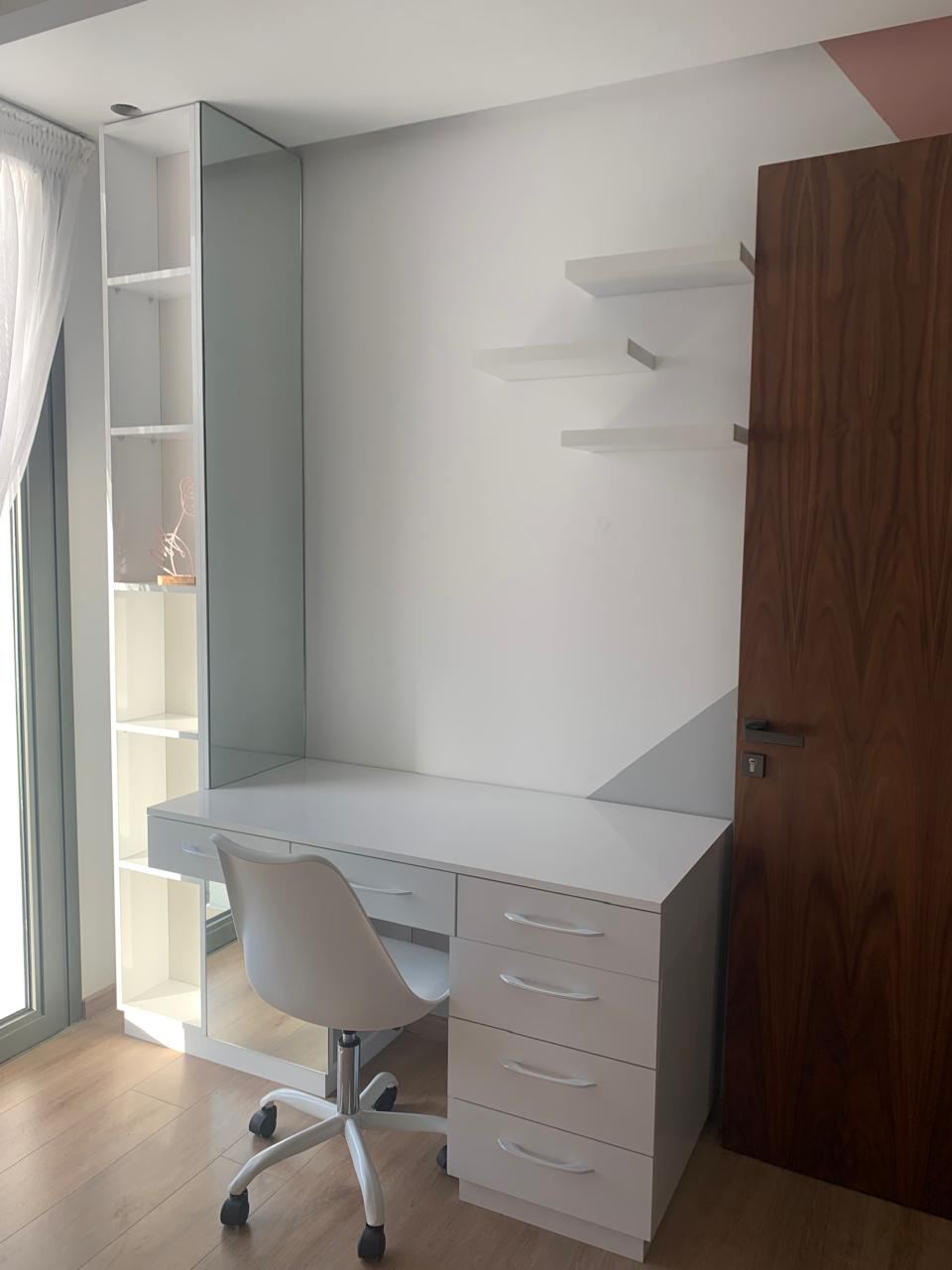 Bureau sur mesure blanc avec caisson à tiroirs, étagères murales et colonne de rangement vitrée, à côté d'une porte en bois foncé.