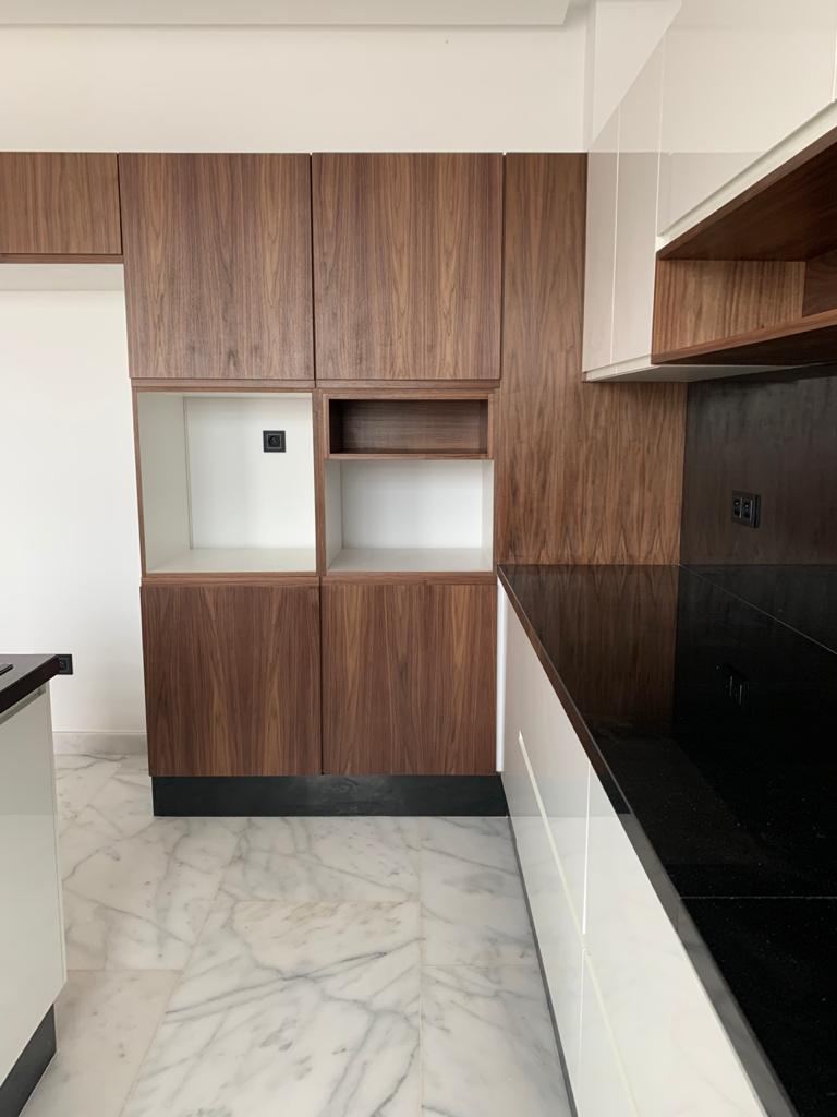 Meubles hauts en bois foncé et niches ouvertes au-dessus d'un plan de travail noir, crédence en verre noir et sol en marbre veiné.