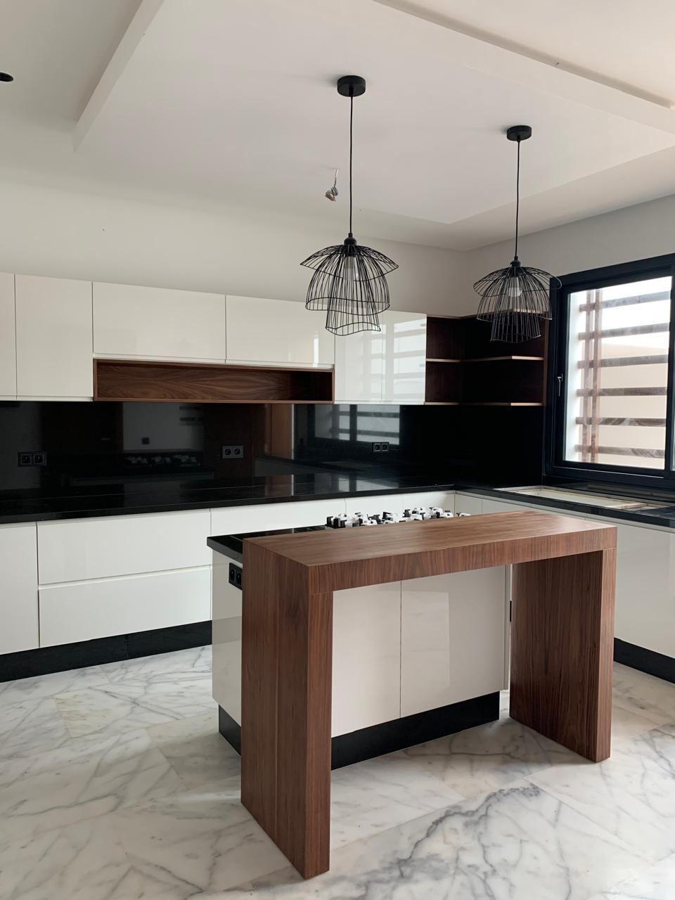 Cuisine sur mesure réalisée par H&L Menuiserie à Kénitra : façades blanches, îlot central en bois foncé, crédence en verre noir et plan de travail en granit.