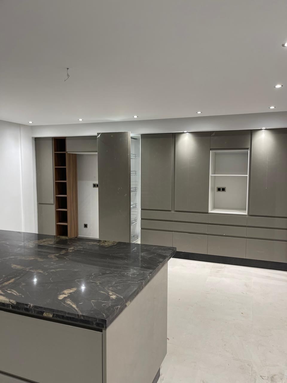 Îlot de cuisine au plan de travail en granit sombre poli, dans une pièce ouverte aux rangements gris toute hauteur.