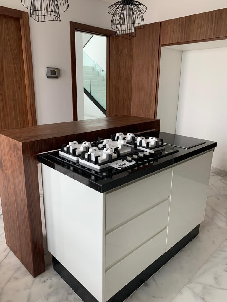 Îlot blanc avec table haute en bois foncé et plaque de cuisson au gaz encastrée, sous deux suspensions noires ajourées.
