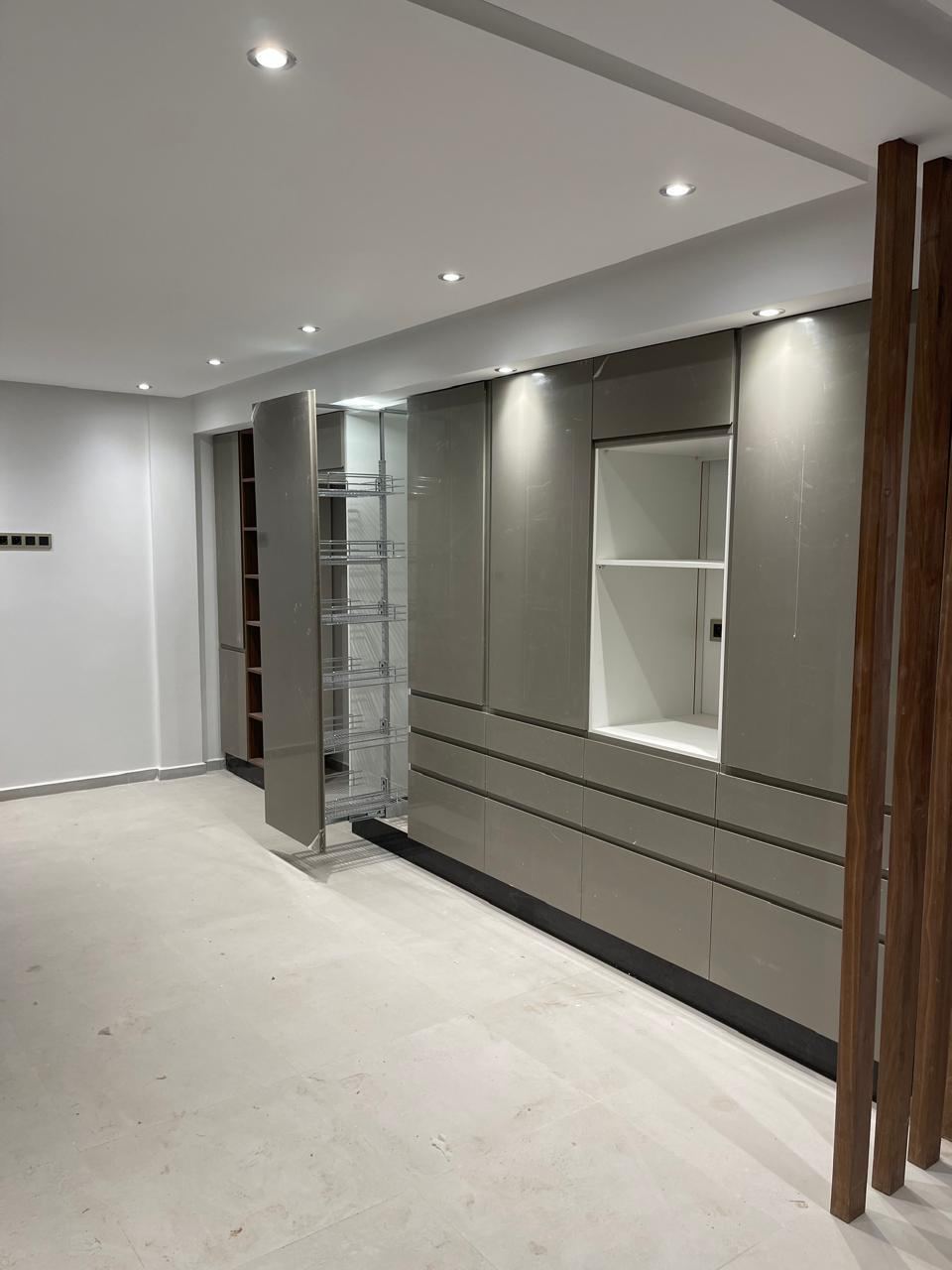 Rangements gris toute hauteur avec niche ouverte, prolongés par un claustra en tasseaux de bois qui sépare la cuisine du séjour.