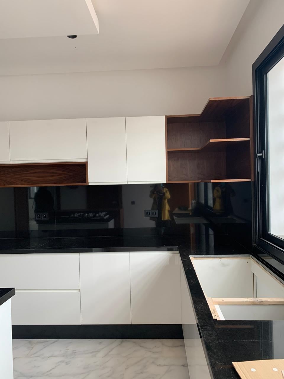Meubles hauts blancs et étagère ouverte en bois foncé au-dessus d'une crédence en verre noir et d'un plan de travail noir.