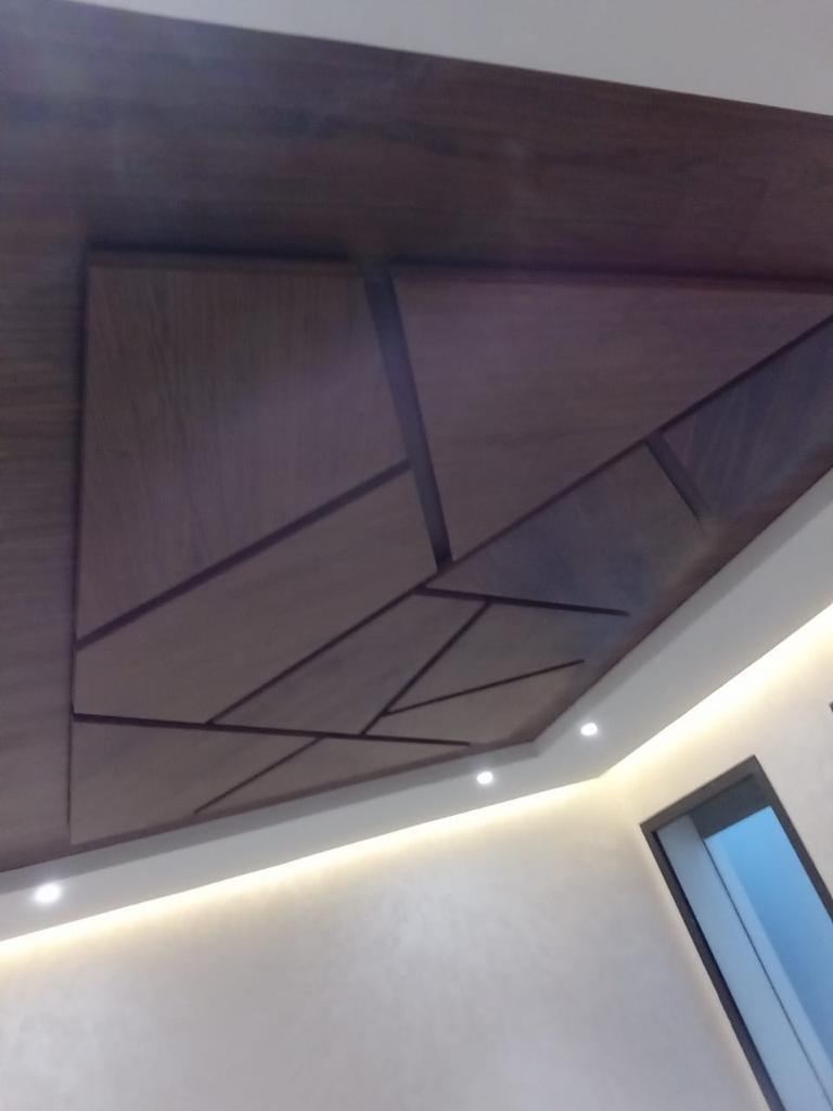 Faux plafond en bois foncé à motif géométrique de lignes brisées, avec éclairage indirect en périphérie.