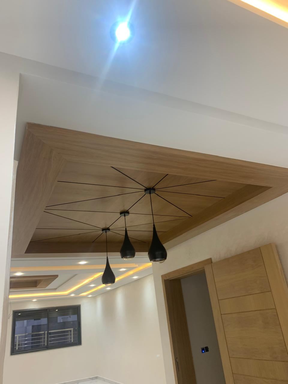 Caisson de faux plafond en bois clair intégrant un motif de fines baguettes croisées et trois suspensions noires.