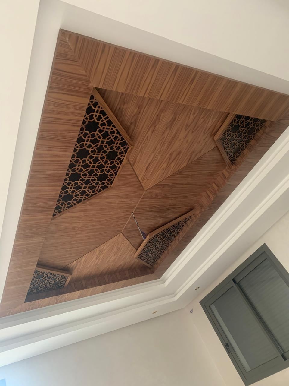 Faux plafond en bois foncé à panneaux rayonnants et incrustations ajourées, encastré dans un plafond blanc.