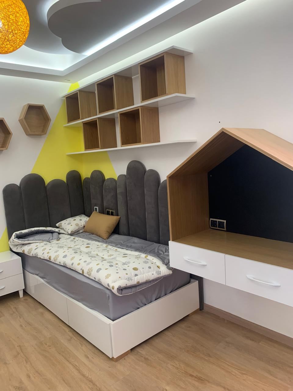 Chambre d'enfant sur mesure : lit avec tiroirs, tête de lit capitonnée, étagères murales et niche en forme de maison.