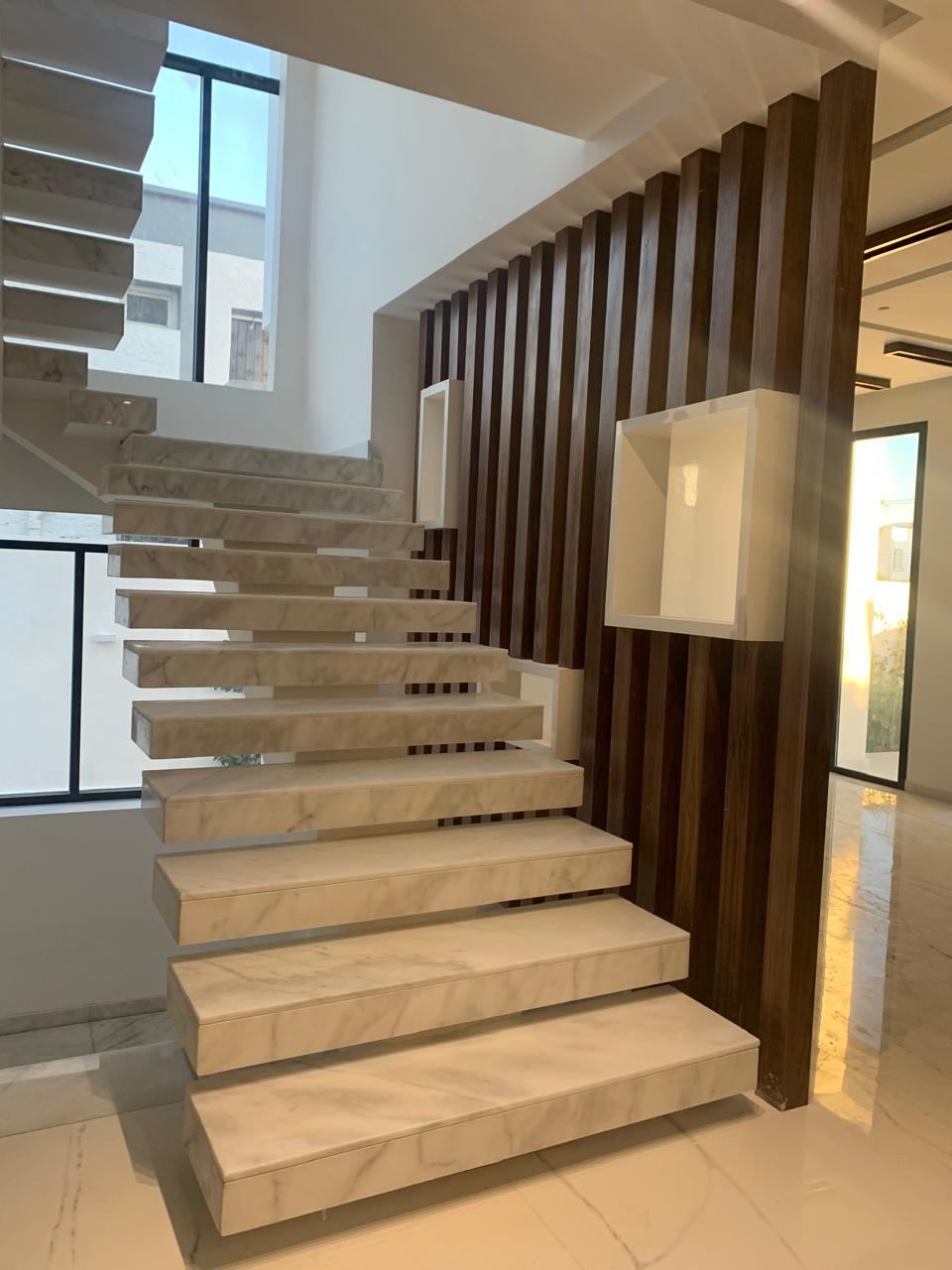 Claustra en tasseaux de bois foncé toute hauteur bordant un escalier en pierre claire à marches suspendues.