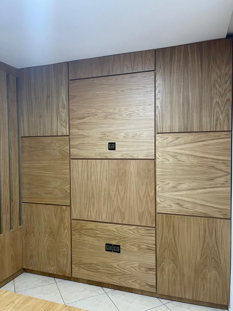 Mur entièrement habillé de panneaux de bois de formats différents, intégrant des portes de placard affleurantes.