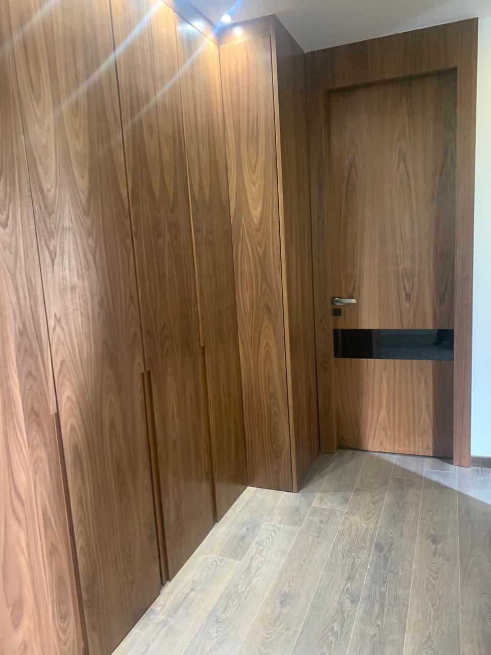 Placard toute hauteur en bois foncé occupant un mur entier de chambre, avec porte intérieure assortie et éclairage encastré.