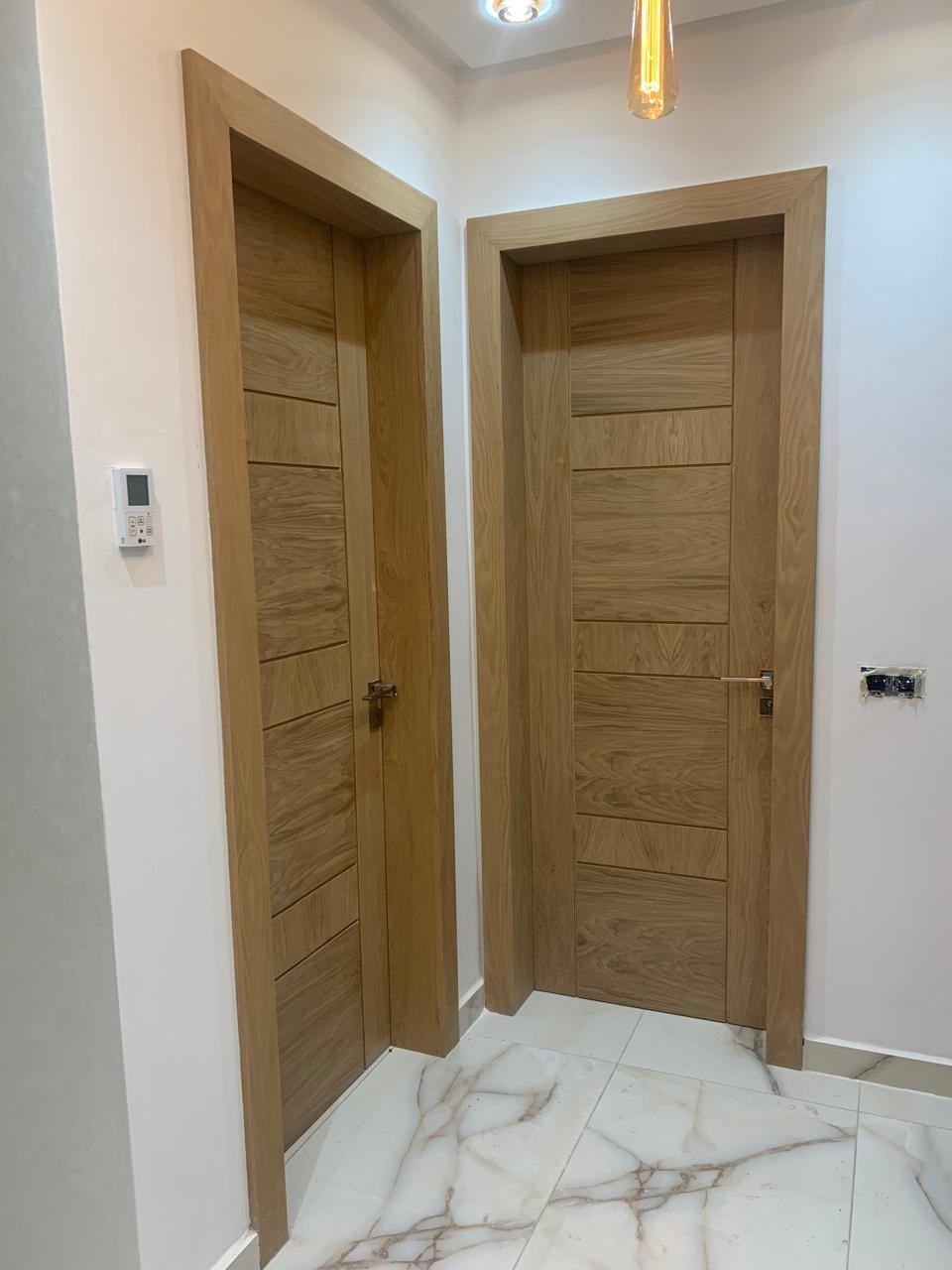 Deux portes intérieures en bois clair à rainures horizontales, encadrements assortis, sur sol en marbre blanc veiné.