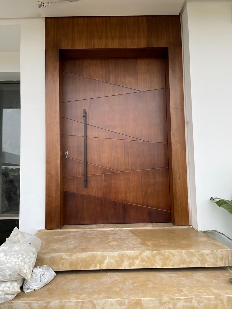 Porte d'entrée en bois foncé à rainures diagonales avec longue poignée verticale, sur un seuil en pierre.