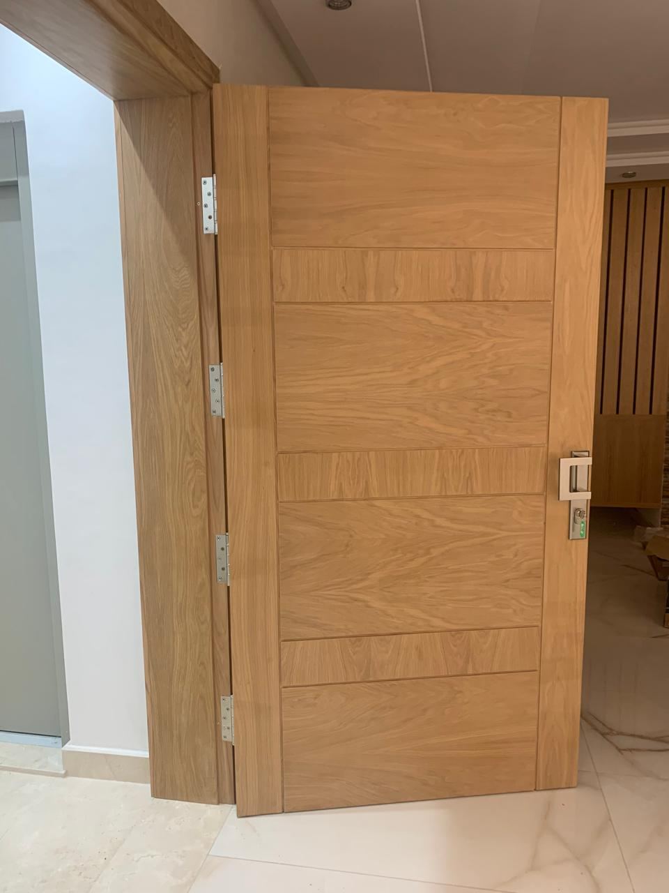 Porte intérieure en bois clair ouverte, panneau à motif géométrique incrusté et serrure encastrée.
