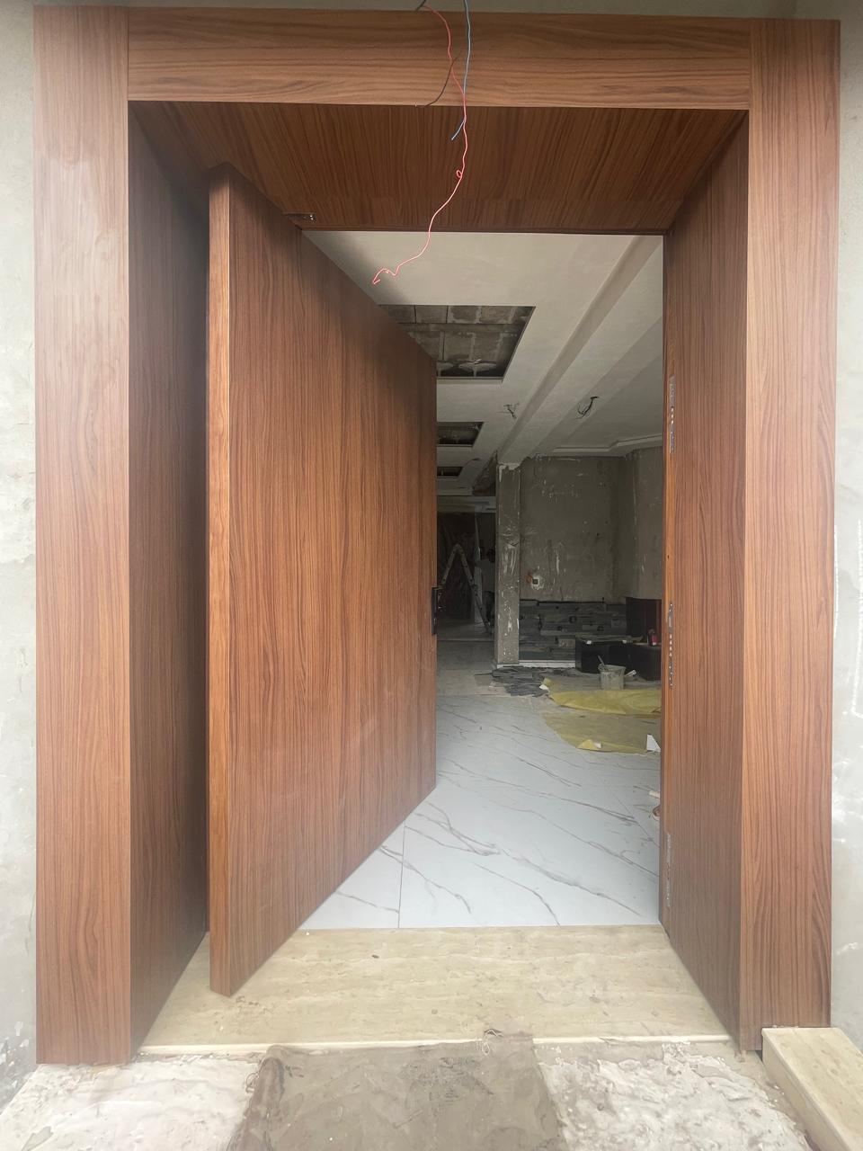 Porte en bois foncé dans un large encadrement assorti, ouverte sur une pièce en cours de finition.