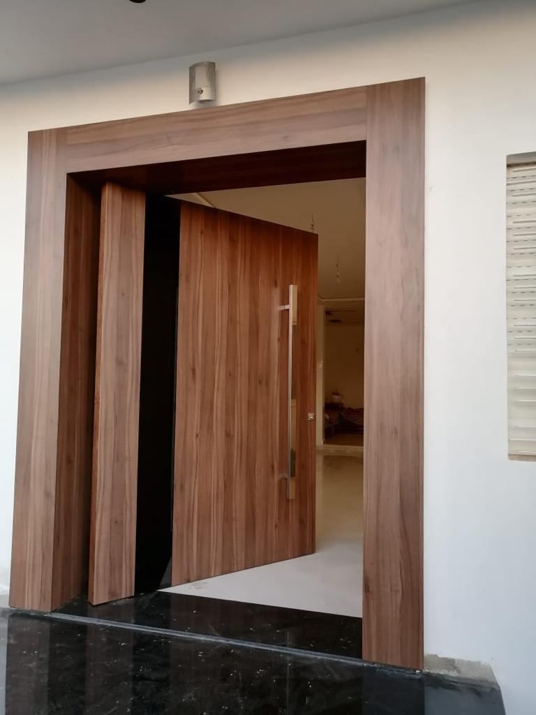 Porte en bois foncé ouverte dans un encadrement large, seuil en marbre noir et pièce claire à l'arrière-plan.