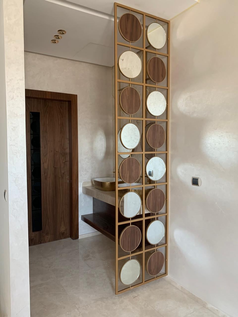 Claustra décoratif toute hauteur à cadres carrés et disques alternés bois et blanc, séparant une entrée d'un couloir.