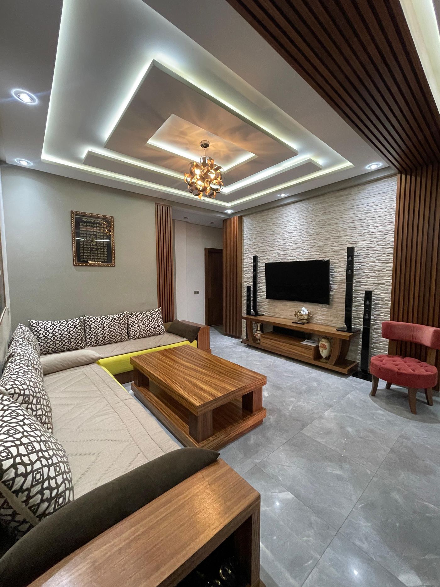 Salon marocain meublé avec banquettes, table basse en bois, meuble TV sur mesure et faux plafond à caissons éclairés.