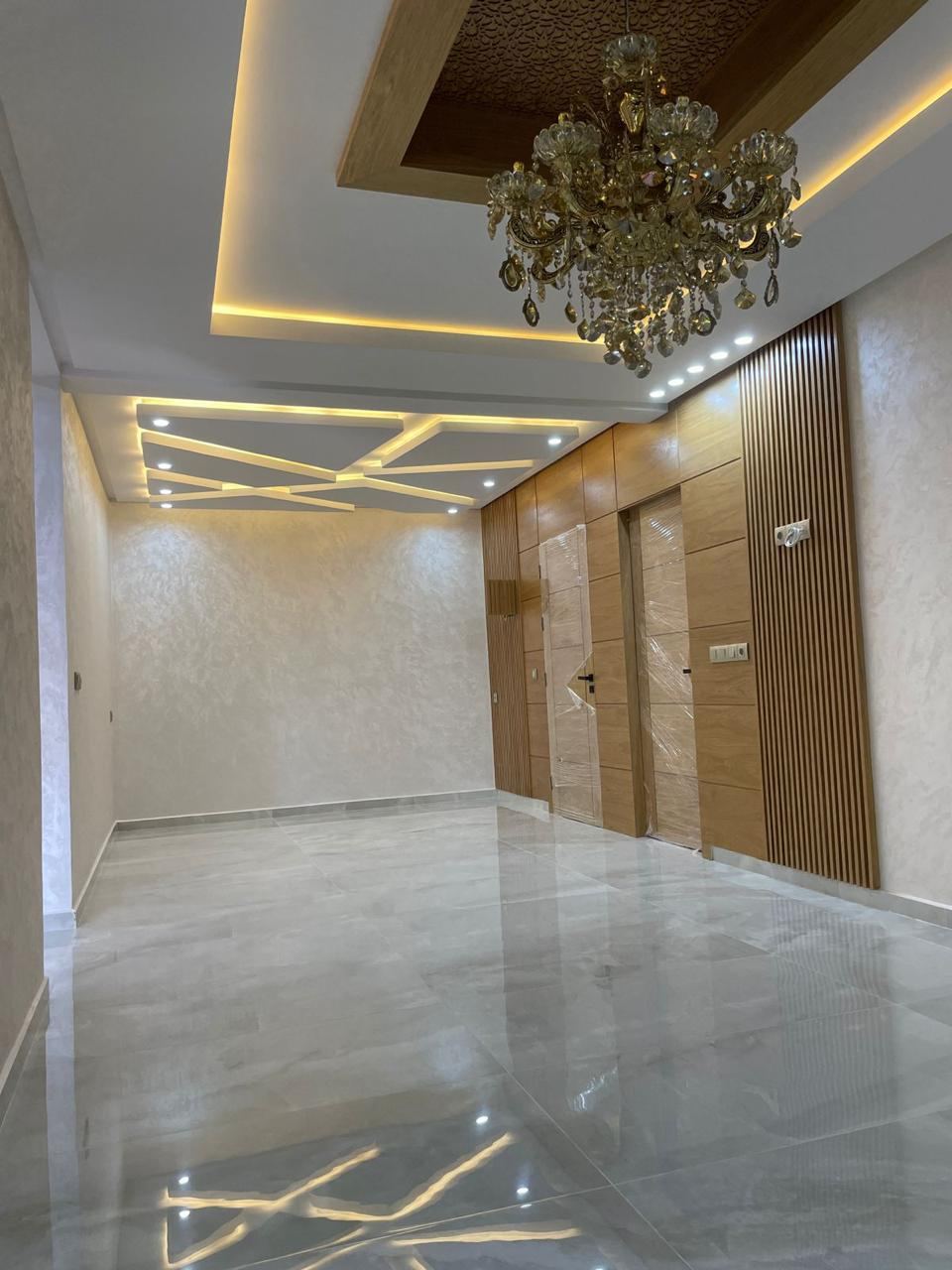 Couloir d'entrée habillé de panneaux de bois clair et de portes assorties, avec faux plafond décoratif et éclairage encastré.
