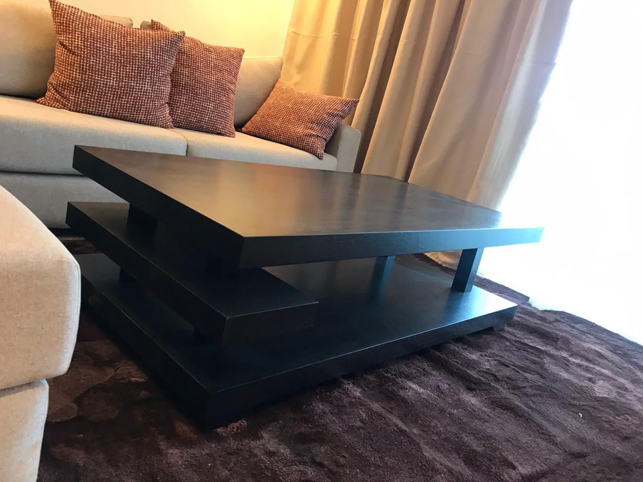 Table basse sur mesure à deux plateaux décalés en bois teinté foncé, posée sur un tapis devant un canapé clair.